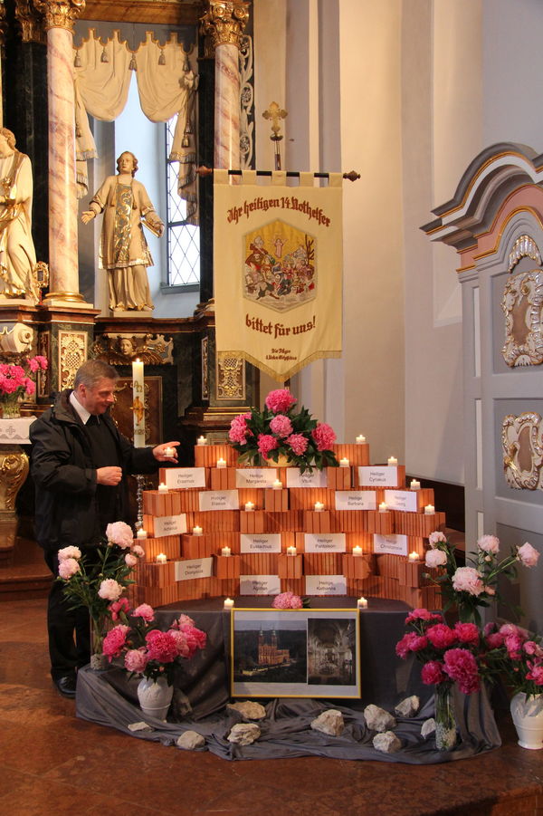 Wallfahrtspfarrer Matthias Kaminski setzt während einer Stellprobe eine Kerze zu den Steinen mit den Namen der 14 Heiligen Nothelfer. Steine, Namensschilder, Kerzen und Fahne werden während der Wallfahrtszeit vom 26. bis 29. Juni in St. Laurentius aufgestellt.